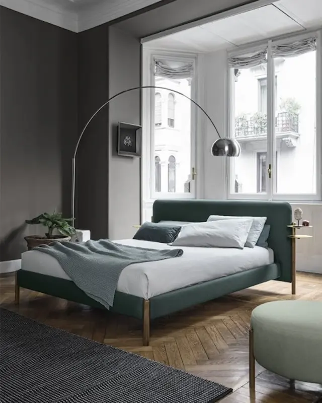 Cama tapizada Flag de Bolzan con estructura de madera, textiles suaves y detalles en latón, en ambiente de dormitorio contemporáneo.